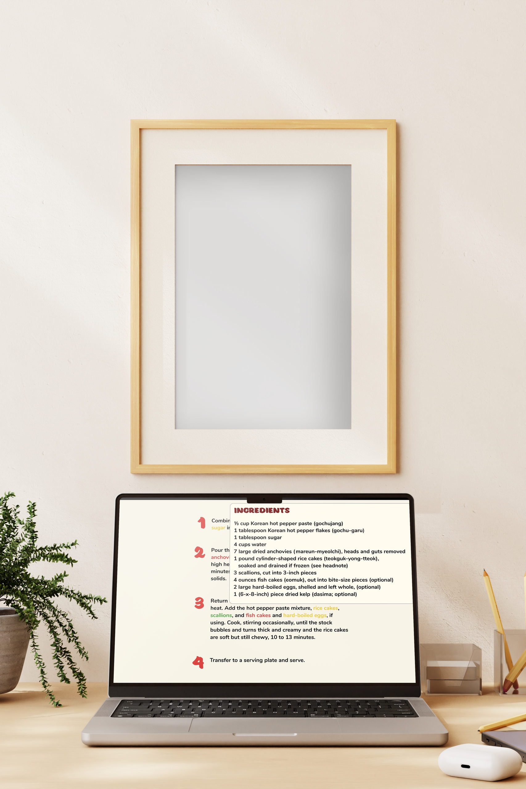 A laptop on a wooden desk showing a recipe page from the site: a numbered INGREDIENTS and method list set in red and black over a pale background.